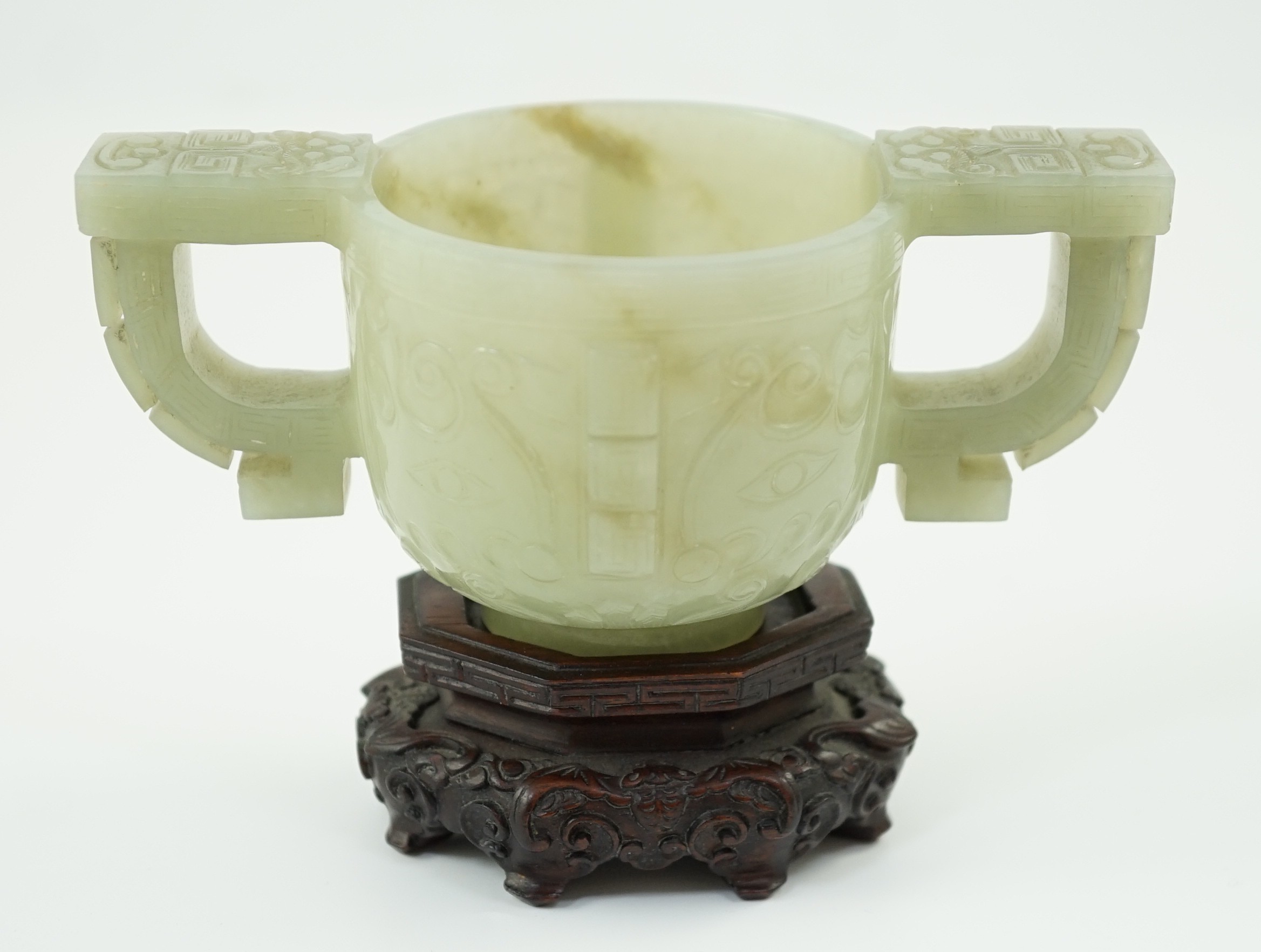 A Chinese archaistic celadon jade two handled cup, 17th century, 12.9cm across 6.1cm high, associated wood stand